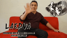 a man sits on a red couch in front of a sign that says laedva on it
