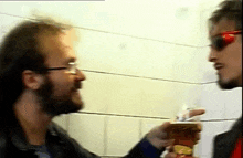 a man wearing sunglasses talks to another man who is holding a can of soda