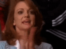 a woman with red hair is clapping her hands and making a funny face .