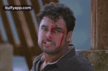 a man with blood on his face is standing in front of a building .