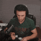 a man wearing headphones and a green shirt that says hawks is sitting in front of a microphone