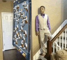 a boy in a suit and bow tie is standing on a set of stairs next to a wall with guns on it .