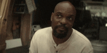 a bald man with a beard wearing a white shirt is looking up