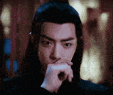 a man with long hair is covering his mouth with his hand