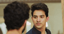 a man is looking at himself in a mirror while another man looks on .