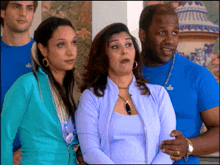 a man wearing a blue shirt with a crown on it stands next to two women