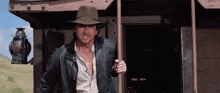 a man in a hat and leather jacket is standing in front of a building .