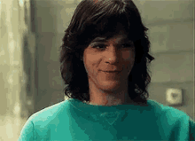 a young man with long hair is wearing a green sweatshirt and smiling .