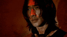 a man with long hair and a black tie has a red spot on his face