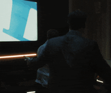 a man in a suit stands in front of a large screen with a blue j on it