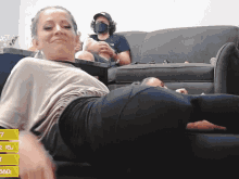 a woman laying on a couch with a man sitting on a couch behind her