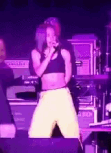 a woman in a crop top is singing into a microphone on stage .