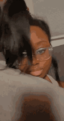 a girl wearing glasses is laying on a bed with her hair in a bun .