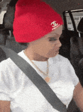 a woman is sitting in a car wearing a red beanie and a white shirt .