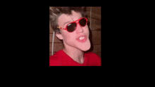 a close up of a person wearing red sunglasses and making a funny face .