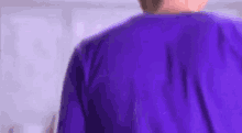 a man in a purple shirt is standing in front of a white wall in a room .