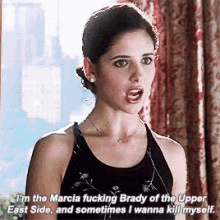 a woman in a black tank top is standing in front of a window and talking to someone .