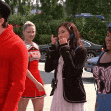 a woman talking on a cell phone with a cheerleader in the background wearing a red cheerleading uniform
