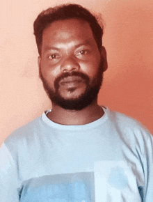 a man with a beard is wearing a light blue shirt with the letter l on it