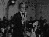 a man in a tuxedo sings into a microphone in front of a crowd