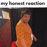 a man in an orange shirt is standing in front of a black curtain with the words `` my honest reaction '' written above him .