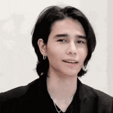 a man with long hair and earrings is wearing a black jacket and necklace .
