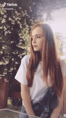 a woman with long red hair is wearing overalls and a white shirt
