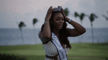 a woman wearing a sash and a crown is standing in front of the ocean .