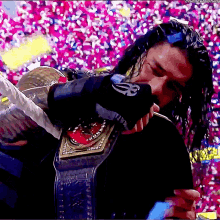 roman reigns is holding a championship belt in front of a crowd of people