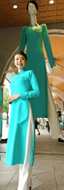 a woman in a turquoise dress is standing next to a mannequin