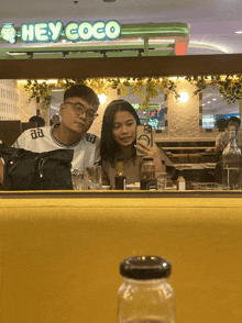 a man and a woman are taking a picture in front of a restaurant called hey coco