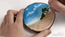a person is painting a picture of a beach on a wooden slice