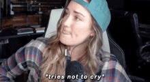 a woman wearing a hat and headphones is sitting in front of a microphone and saying `` tries not to cry '' .