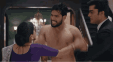 a shirtless man is being held by a woman in a purple dress