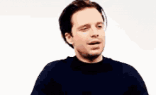 a man in a black sweater is making a funny face while looking at the camera .