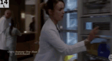 a woman in a white lab coat is reaching into a refrigerator .