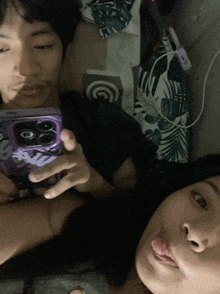 a man and a woman are laying on a bed and the man is holding a phone with a case that says barbie on it