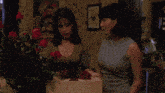 two women are standing next to each other in front of a vase of roses