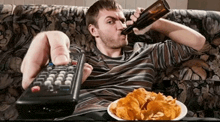a man sitting on a couch drinking a beer and eating chips
