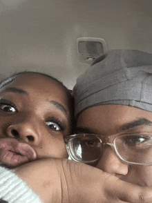 a woman wearing glasses and a gray hat holds her hand to her face next to another woman