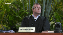 a man sitting at a desk with a sign that says verteidiger on it