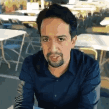 a man with a beard is sitting at a table in front of tables .