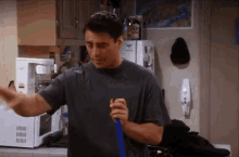 a man in a grey shirt is holding a blue mop in a kitchen .