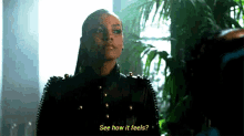 a woman in a black leather jacket is standing in front of a plant and talking to someone .