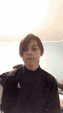 a young boy is wearing a black adidas sweater and making a funny face .
