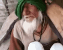 a man with a beard and a green turban is sitting on a chair .