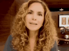 a woman with curly hair is looking at the camera with a cross in the background