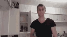 a man in a black shirt is standing in front of a kitchen cabinet