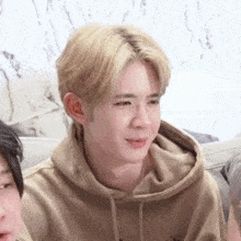 a young man with blonde hair is wearing a tan hoodie .