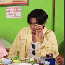 a man in a yellow shirt is sitting at a table with a pepsi glass